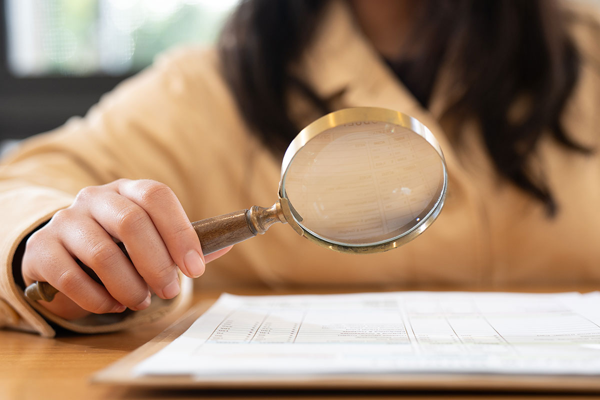 woman holding magnifying glass looking for errors in document